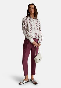 Blouse blanche à manches longues avec broderie florale bordeaux, associée à un pantalon bordeaux, des sandales argentées et un petit sac à main blanc.