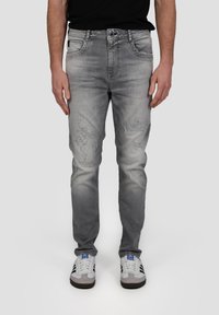Jean en denim gris avec des patches déchirés, coupe slim, design à cinq poches et fermeture à bouton, accompagnés de baskets blanches.
