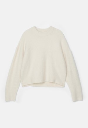 Ullgenser i off-white med rund hals, senket skuldre og en kortet hem. Myk tekstur med en løs passform.