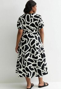 Robe noire et blanche jusqu'aux genoux avec une coupe ample, des manches bouffantes et un motif abstrait. Le tissu semble léger avec une texture lisse.