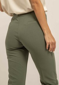Pantalons ajustés verts olive en tissu lisse, avec une taille mi-haute, deux poches arrière et une silhouette fuselée.