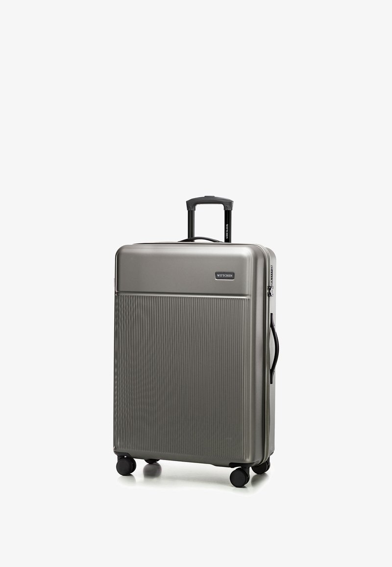 Srebrna twarda walizka z rowkowaną teksturą, czarnymi kołami i teleskopową rączką. Posiada płytkę z logo z przodu.