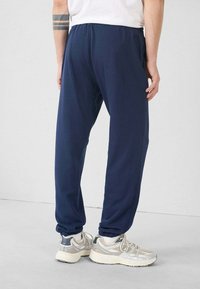 Pantalones deportivos azul marino con un corte relajado, cinturilla elástica y tobillos ajustados, combinados con zapatillas grises y blancas. Textura suave.