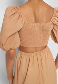 Smockad crop-top i beige med puffärmar, med fyrkantig halsringning och öppen ryggdesign. Tyget är lätt och texturerat.