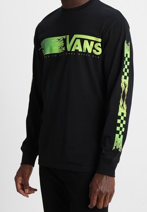 Czarna koszula z długim rękawem z neonowo zielonym logo Vans i motywami płomieni na piersi i rękawach, noszona przez osobę o ciemnej karnacji.