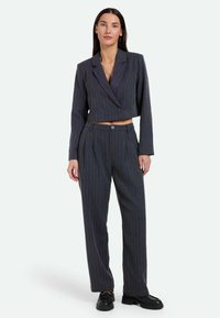 Blazer corto grigio scuro con righe verticali, chiusura a singolo bottone e pantaloni a vita alta coordinati; entrambi realizzati in tessuto testurizzato.