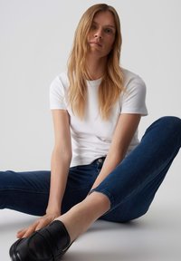 T-shirt blanc à manches courtes, design ajusté. Jean en denim bleu foncé avec un ourlet retroussé. Mocassins noirs avec une texture lisse. Style minimaliste.