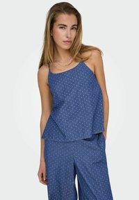 Blauwe denim top met een losse pasvorm, dunne bandjes en een patroon van kleine witte stippen. In combinatie met bijpassende blauwe onderkant.