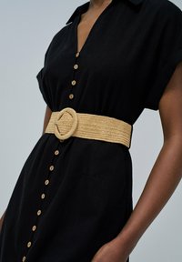 Schwarzes Hemdkleid mit kurzen Ärmeln und Holzknöpfen, tailliert mit einem breiten, geflochtenen Strohbelt mit einer runden Schnalle.