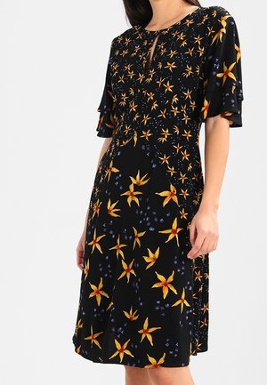 Robe noire mi-longue aux motifs floraux en forme d'étoile jaunes et orange, manches courtes à volants et petit décolleté en forme d'œillet.