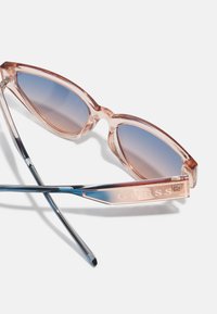 Occhiali da sole a forma di occhio di gatto con montatura rosa traslucida, lenti blu con gradiente, dettagli in metallo argentato e logo sulla stanghetta.