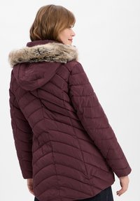 Bordeaux pufferjack met een gewatteerd ontwerp, voorzien van een met faux fur gevoerde capuchon en verticale naden voor een slanker uiterlijk.