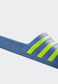 Plave Adidas klizne sandale s tri jarke zelene pruge na remenu i teksturiranom površinom potplata.