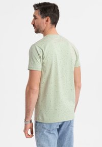 Camiseta verde claro de manga corta, con un patrón salpicado de puntos más oscuros. Fabricada en una tela suave, tiene un diseño clásico de cuello redondo.