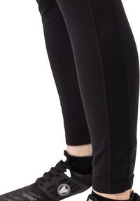Zwarte sportleggings met een aansluitend ontwerp, textuurpanelen aan de zijkanten en versterkte naden, gecombineerd met zwarte sportschoenen.