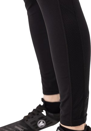 Leggings de sport noirs avec un design ajusté, des panneaux latéraux texturés et des coutures renforcées, associés à des chaussures de sport noires.