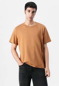 T-shirt marron à manches courtes en coton doux, avec un col rond et une coupe décontractée. Associé à un jeans foncé, avec des détails minimalistes.