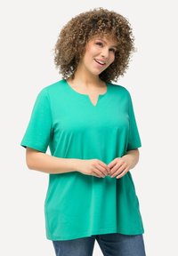 Maglietta verde a maniche corte con scollo a V, realizzata in tessuto morbido, caratterizzata da una vestibilità rilassata e un design casual, abbinata a jeans di denim.