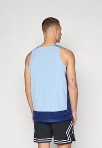 Lys blå mesh tanktopp med marineblå detaljer, som har en pustende tekstur og en avslappet passform. Kombinert med svarte shorts med hvite kanter.