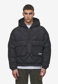 Giacca a vento nera trapuntata con cappuccio, due tasche frontali, chiusura con zip e polsini elasticizzati. Presenta un patch con il logo sulla tasca sinistra.
