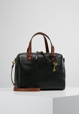 Zwarte leren handtas met bruine handvatten en riem, gouden sleutelbedel en ritssluiting, tentoongesteld op een wit voetstuk.