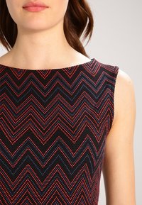 Robe sans manches avec une base noire, présentant un motif en zigzag rouge et bleu. Texture lisse et encolure ronde.