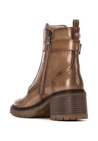 Botín de tobillo de charol marrón con tacón grueso, cremallera lateral y acabado texturizado. Presenta un tacón de madera apilada y suela resistente.