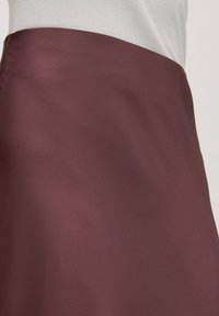 Bordeaux satijnen rok met een gladde textuur, voorzien van een hoge taille. Minimalistisch uiterlijk, reikt tot halverwege de bovenbenen.