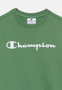 Groene katoenen T-shirt met een ronde hals en korte mouwen, met een opvallend wit "Champion" logo dat over de borst is gedrukt.