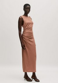 Mauve ärmelloses Kleid mit seitlicher Raffung, aus weichem Stoff, knöchellang und kombiniert mit schwarzen Sandalen mit Absätzen.