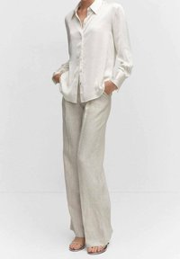 White long-sleeve button-up shirt with a relaxed fit, paired with light beige pleated wide-leg trousers. Sandals feature thin straps.