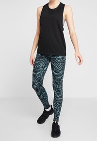 Svart ärmlös topp i kombination med teal- och svartrandiga leggings i zebramönster. Leggingsen har en tajt passform och en texturerad design. Svarta träningsskor.