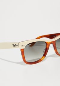Ray-Ban aurinkolasit, joissa on kilpikonnakuosiset kehykset, vaalean kermaiset vartaat, tummanharmaat linssit ja hopeiset logokoristeet temppeleissä.