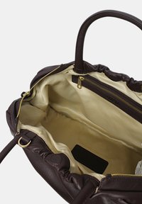 Bolso de mano de cuero marrón con un diseño fruncido. El interior presenta un forro beige, un bolsillo con cremallera y una etiqueta de la marca. Acentos de herrajes dorados.