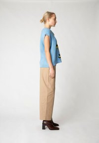Blå stickad ärmlös topp med lös passform, kombinerad med beige vida byxor och mörkbruna klackade ankelstövlar, i sidovy.