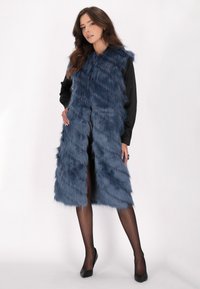 Marinblå faux fur-väst med en lång, rak passform, med hög krage och utan synliga knäppningar, bärs över en svart topp och strumpbyxor.