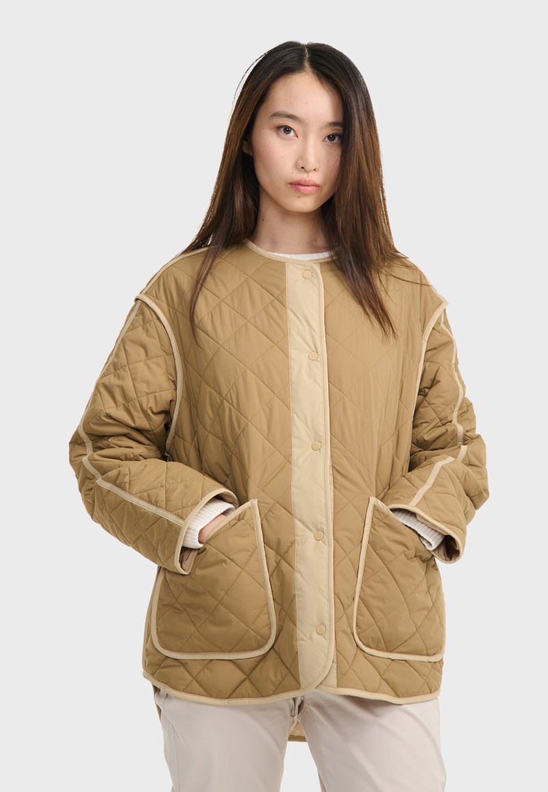 Beige gesteppte Jacke mit Druckknopfverschluss, kontrastierendem hellbeigem Besatz, großen Seitentaschen und lässiger Passform. Strukturierter Stoff mit sichtbaren Nähten.