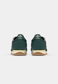 Green suede sneakers with a white midsole and gum rubber outsole. Features classic three-stripe design and logo on the heel.
