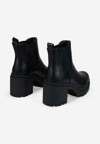 Botas de tobillo de cuero negro con paneles laterales elásticos, suelas de plataforma negras gruesas y tiradores en la parte posterior para facilitar su uso.