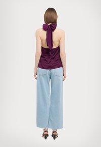 Top in raso viola con un grande fiocco sul retro, abbinato a jeans a gamba larga azzurri con orli sfrangiati e sandali con tacco neri.