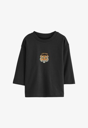 Zwarte katoenen T-shirt met een ronde halslijn en driekwart mouwen. Heeft een geborduurde tijgerkop en "WILD ONE" erboven in oranje tekst.