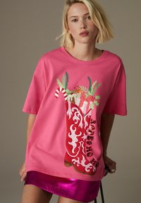 Oversized lyserød t-shirt med et ferietema boot-design med slikstænger og gaver. T-shirten har en glat tekstur og rund hals.