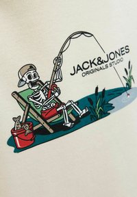 Graphique d'un squelette pêchant depuis une chaise. Le design présente un seau rouge, des poissons et des roseaux, imprimé sur un fond beige clair.