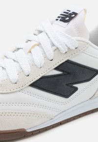 Witte sneaker met een gestructureerd zwart logo. Bevat een mix van lederen en suede materialen, ronde witte veters en een rubberen zool.