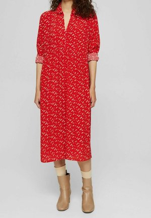 Femme portant une robe midi rouge à manches longues avec de petits motifs beiges, associée à des bottines beiges et des chaussettes claires.