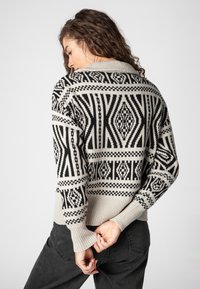 Strickpullover in Beige und Schwarz, mit geometrischen Mustern, hohem Kragen und gerippten Bündchen, in taillierter Passform.