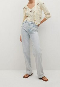 Jasnoniebieskie, wysokogatunkowe dżinsy o luźnym kroju, zestawione z kremowym swetrem robionym na drutach, zdobionym kwiatowymi akcentami, oraz dopasowanym topem na ramiączkach.