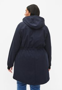 Námornícky modrá parka bunda s regulovateľným pásom, kapucňou, dlhými rukávmi a elastickými manžetami. Hladká textúra a dĺžka po kolená.