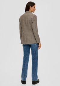 Brauner kariertes Blazer mit taillierter Passform, ausgestattet mit einem einzelnen Kragen und einer glatten Textur. Kombiniert mit blauen Schlagjeans und schwarzen klobigen Stiefeln.