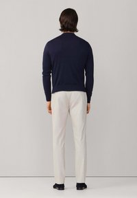 Marineblauwe trui met ronde hals, gecombineerd met lichtgekleurde broek. De stof heeft een gladde textuur met lichte ribbels aan de zoom en manchetten. Donkere schoenen zichtbaar.